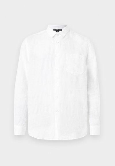 Λευκό πουκάμισο με μακριά μανίκια και κουμπιά, με τσέπη στο στήθος και μυτερό γιακά, σε απλό ανοιχτό γκρι φόντο.