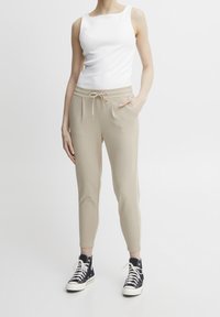 Beiga joggers med elastisk midjeband, dragsko och sidofickor, kombinerade med en vit ärmlös topp och svarta högklackade sneakers.