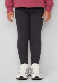 Dunkelgraue Leggings aus einem dehnbaren Baumwollmix, mit einer schmalen Passform und ergänzt durch weiße Sportsneaker mit grauen Akzenten.
