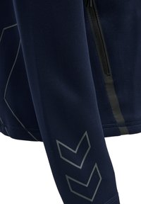 Granatowa kurtka sportowa o eleganckim wyglądzie, matowym wykończeniu, widocznych detalach przeszycia oraz odblaskowych szarych akcentach na rękawach.