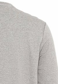 Grå tekstureret langærmet top med rund halsudskæring og enkelt design, der fremhæver et blødt strikstof og fine mønstre.