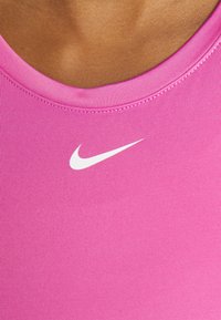 Top deportivo rosa de textura acanalada y escote ancho. Presenta un logo de Nike en blanco en la parte frontal. Tejido suave.