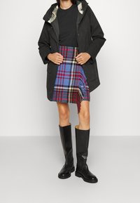 Black lightweight jacket with a hood, layered over a black shirt and a blue plaid skirt with red and yellow lines. Knee-high black boots.