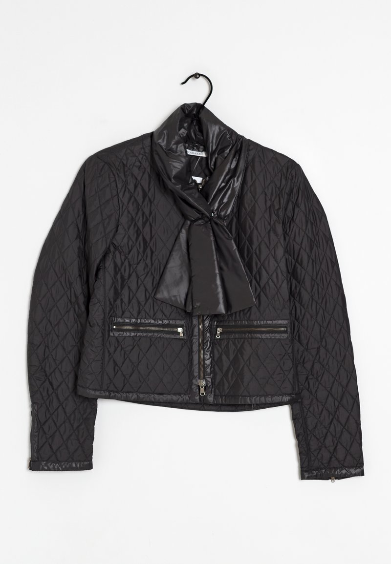 Veste matelassée noire avec une fermeture éclair à l'avant, deux poches zippées et un détail noué en forme d'écharpe autour du col, suspendue sur un cintre.
