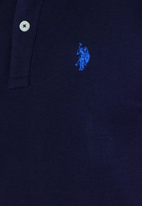 Navy polo shirt featuring a blue embroidered logo of a polo player riding a horse. Two buttons visible on the collar.