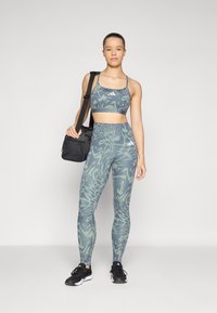 Bra sportivo e leggings in grigio-verde chiaro con motivi astratti; abbinati a una borsa nera e scarpe da corsa nere.