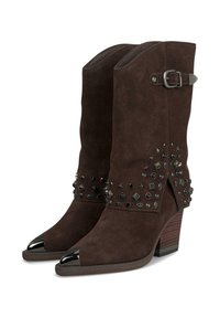 Botas de tobillo de ante marrón con punteras negras en forma de punta, detalles de tachuelas, acento de hebilla y un tacón apilado. Corte decorativo en los laterales.