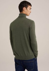 Pulover verde cu guler înalt, realizat dintr-un material moale, cu mâneci lungi și un design ajustat, asortat cu blugi negri pentru un look casual.