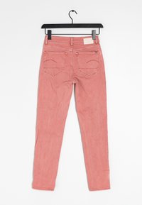 Jeans skinny rosa exhibidos colgados en una percha negra. Presentan cinco bolsillos, detalles de costura y una textura suave.