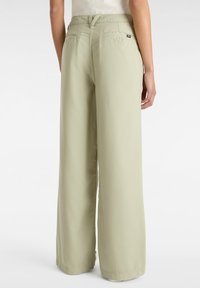 Pantaloni a gamba larga verde chiaro con una texture liscia e morbida. Presentano due tasche posteriori e una piccola etichetta del marchio vicino alla vita.