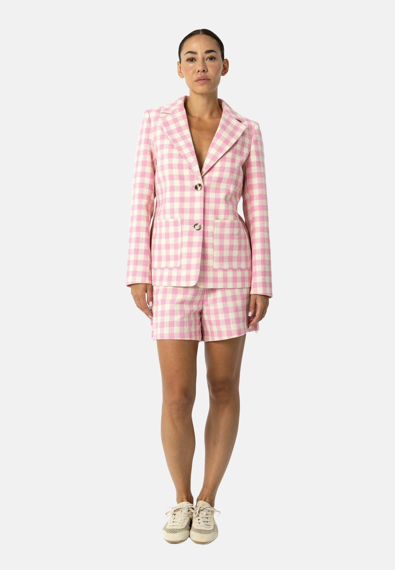 Blazer à carreaux roses et blancs avec short assorti. Le blazer présente un col cranté et deux poches avant, fini avec des boutons argentés.