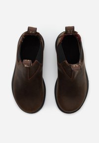 Botas de tobillo de cuero marrón con paneles laterales elásticos. Punta redondeada, suela de goma negra y forro a cuadros en contraste. Incluye lengüetas de tirón.