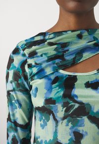 Hodně dlouhý rukáv s abstraktním vzorem v zelené, černé a modré barvě. Obsahuje volný výstřih a detail s výřezem s hladkou texturou.