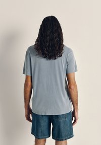 Light blue cotton t-shirt with short sleeves and a relaxed fit, paired with denim shorts. Simple design, no visible patterns or accents.