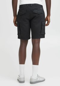 Shorts cargo negros con bolsillos laterales, bolsillos traseros planos y un ajuste clásico. Combinados con zapatillas grises y calcetines blancos.