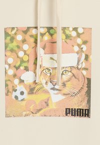 Kanva krepšys su grafika, kurioje pavaizduotas katinas Kalėdų skrybėlėje, o fone matomi susilieję Kalėdų šviesos ir futbolo kamuolys. Spalvos yra šiltos ir ryškios.