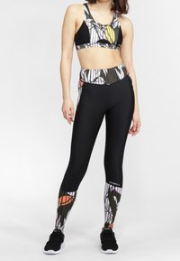 Top sportivo nero con un motivo astratto multicolore, abbinato a leggings neri con un design simile sulla parte inferiore delle gambe. Sneakers nere.