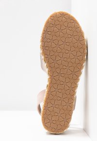 Sandale rose avec une semelle en caoutchouc texturé arborant un motif d'étoiles, un contour en jute tissé et une sangle ajustable pour un maintien sécurisé.