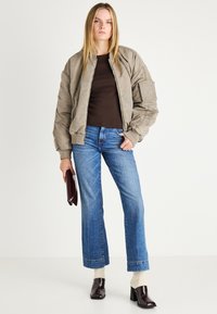 Khaki bomberska jakna z ribastimi manšeti, kombinirana z dolgimi rjavimi rokavi in modrimi širokimi kavbojkami. Model nosi temno torbico in sijoče pete.