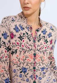 Knit cardigan with a floral pattern in pink, blue, and green. Features a rounded collar and five green buttons down the front.