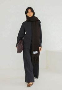 Écharpe en laine sombre avec des franges, assortie à une chemise à rayures et un pantalon à jambes larges. Un sac en cuir et des ballerines à imprimé léopard complètent le look.
