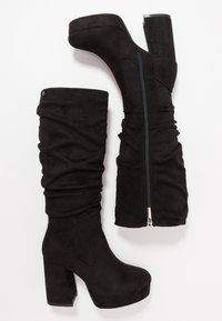 Botas negras por encima de la rodilla en suave ante con un diseño relajado, que presentan un cierre lateral y un tacón grueso. La textura es suave con mínimos acentos.