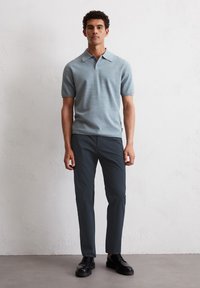 Jasnoniebieska koszulka polo z krótkim rękawem i kołnierzykiem, w połączeniu z ciemnoszarymi zwężającymi się spodniami i czarnymi sznurowanymi butami.