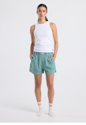 White sleeveless tank top paired with green and white gingham shorts. Shorts feature an elastic waistband and front pockets. Plain white socks with orange stripes.
