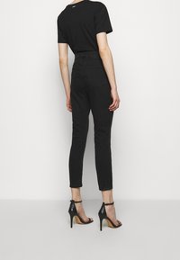 Svarta figurnära jeans med hög midja, i kombination med svarta klacksandaler med remmar. Slät och mjuk tyg med en elegant design, utan synliga mönster.