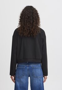 Czarna krótka bluza z długimi rękawami, ściągaczem u dołu i opuszczonymi ramionami, zestawiona z niebieskimi dżinsami z tylnymi kieszeniami.