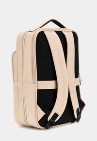 Zaino beige con un design strutturato, dotato di spallacci in rete nera, tessuto testurizzato e doppi zip laterali.