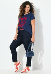 Námořnické modré tričko s červeným textem, skinny kalhoty s puntíky, červeno-bílé tenisky a malá modrá kabelka. Neformální design oblečení.