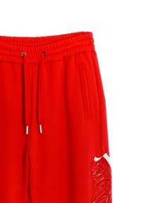Pantalones de chándal rojos con un tejido texturizado, cintura elástica, cordón ajustable y un diseño de ala bordado en el lado izquierdo.
