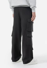 Black cargo pants made of cotton with a relaxed fit. Features include side cargo pockets and a smooth texture. Worn with white sneakers.