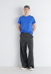 Camiseta de algodón azul, pantalones de pierna ancha grises con cintura elástica, zapatillas de deporte en blanco y negro, y una gorra gris. Conjunto simple y casual.
