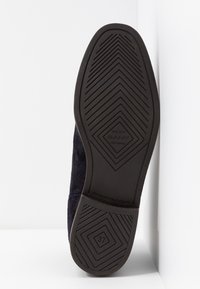 Donkerblauwe suède schoen met een gestructureerde zwarte rubberen zool met een geometrisch profiel. Maatlabel vermeldt 37. Gladde, strakke uitstraling.