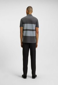 Węglowy polo z szarymi poziomymi paskami, krótkimi rękawami i klasycznym kołnierzykiem, zestawione z czarnymi spodniami i ciemnymi butami.