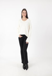 Pull en tricot blanc épais avec un décolleté large et des épaules tombantes, associé à un pantalon noir évasé et des bottines noires à bout pointu.