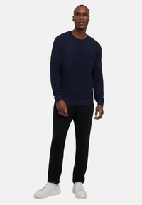 Marineblauwe gebreide trui met een ronde hals, gecombineerd met zwarte pantalons en witte sneakers. De stof lijkt zacht en aansluitend met een geribde tailleband.