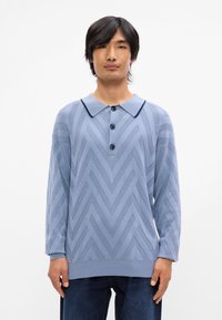 Pull en tricot bleu clair avec un motif en zigzag, col et trois boutons. Doté de manches longues et d'un ourlet côtelé.