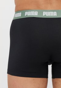 Black cotton boxer shorts with a green waistband featuring the "PUMA" logo in white. The fabric appears smooth and fitted.