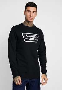 Sudadera negra de manga larga con un logotipo blanco de Vans en el frente, con puños acanalados y cuello redondo. Tejido suave, corte casual.