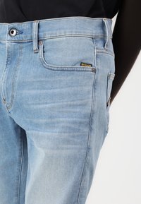 Jeans in denim blu chiaro con un leggero effetto usurato, caratterizzati da un'etichetta di marca, design a cinque tasche e chiusura con bottone metallico.