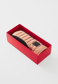 Προστατευτικό καρπού με επένδυση από καφέ και μαύρο ύφασμα σε ορθογώνιο σχήμα, παρουσιασμένο σε φωτεινό κόκκινο κουτί. Διαθέτει ετικέτα λογότυπου στο πλάι.