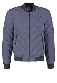 Námořnická prošívaná bomber bunda s kulatým výstřihem, zipovým zapínáním, bočními kapsami a žebrovanými manžetami a lemem. Na hrudi je malá nášivka.