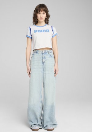 Camiseta blanca cortada con detalles en azul y logo "PUMA", combinada con jeans de pierna ancha en azul claro. Tejido suave y corte holgado.