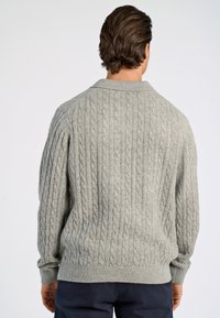 Harmaa kierteinen neulepaita, jossa on ribbikuvio hihansuissa ja helman osassa, sekä teksturoitu kuvio. Klassinen kaulustyyli ja hieman väljä muotoilu.