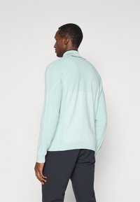 Ανοιχτό μπλε πουλόβερ με ψηλό γιακά, υφαντές λωρίδες στα μανίκια και λεία επιφάνεια. Φορεμένο πάνω από σκούρα παντελόνια, με θέα από πίσω.