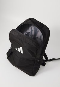Zaino in nylon nero con tasca frontale con zip, tasche laterali in rete e logo riflettente. Interno grigio con scomparti spaziosi.