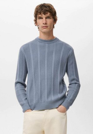 Suéter azul claro tejido con patrón acanalado, escote redondo y mangas largas, combinado con pantalones color crema. Textura suave evidente.